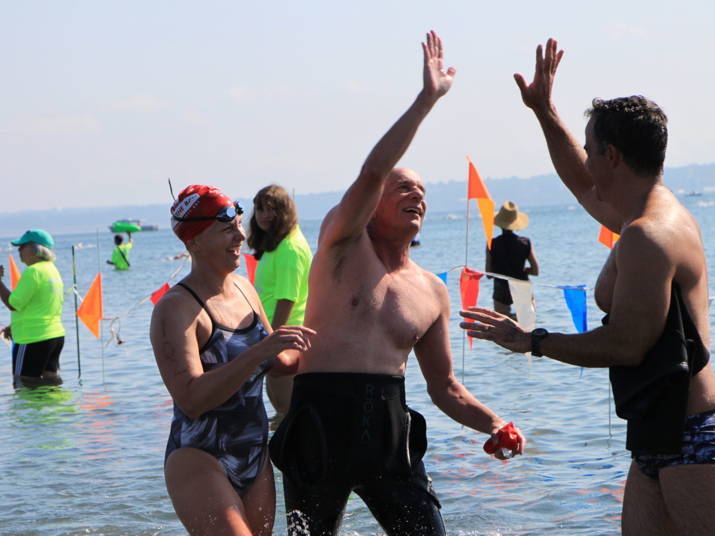 Three swimmers high-five their congratulations at the finish line of the Save The Bay Swim 2022