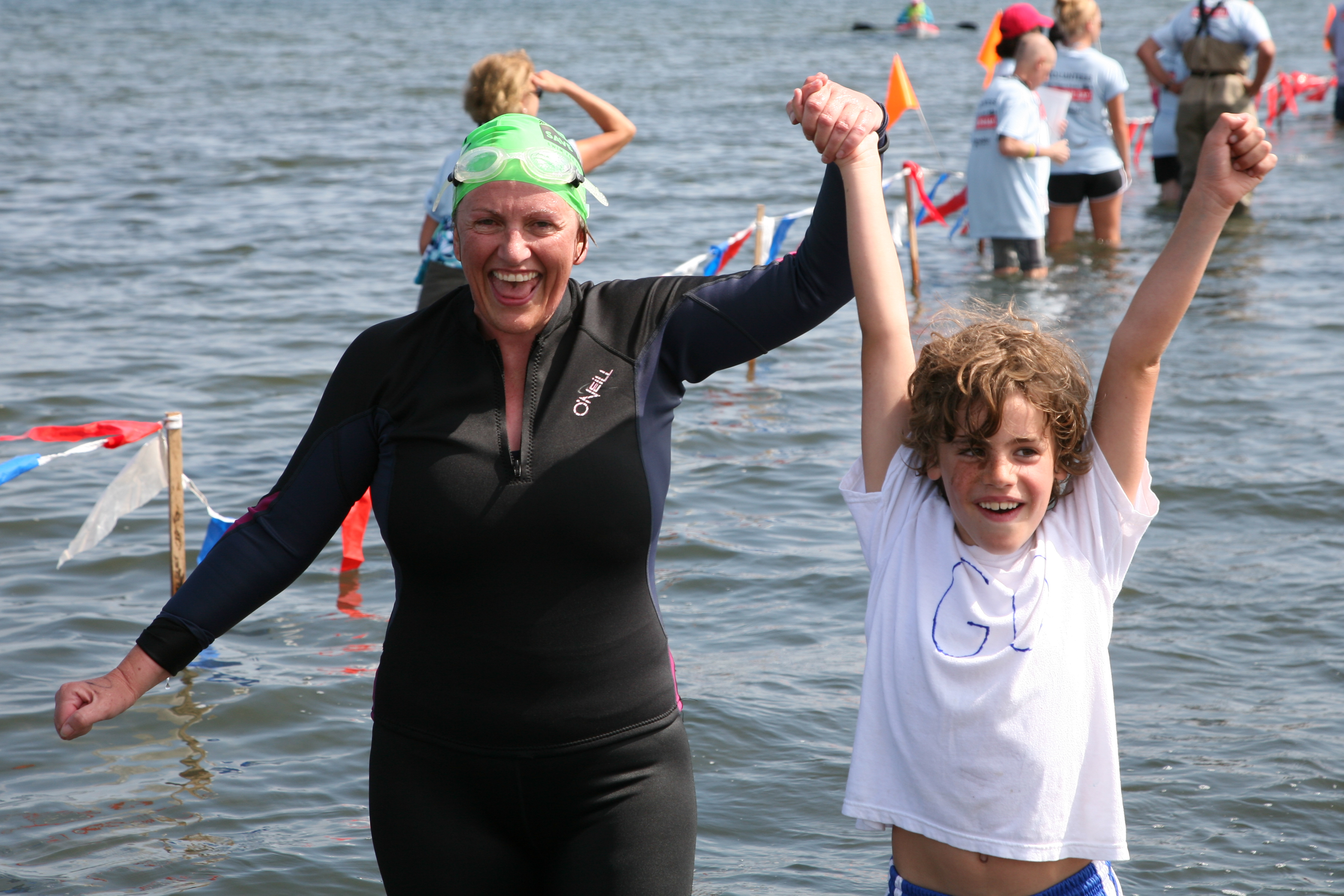A woman in a wetsuit emerges from the finish funnel at Save The Bay's annual Swim fundraiser, holding the hand of a young boy who is cheering for her.